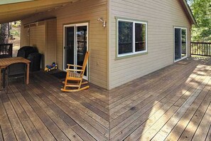 A wooden deck with a rocking chair and a table, a sliding glass door, and a window. - Bigfoot Cabin - Big Trees Village (Camp Connell)