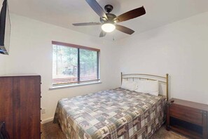 Ein Schlafzimmer mit einem Bett, einem Deckenventilator, einem Fenster mit Jalousien und einer hölzernen Kommode.