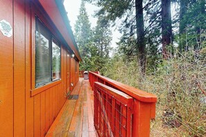 Une cabane en bois dotée d’une terrasse, entourée de grands arbres.