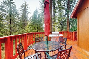 Eine Holzterrasse mit rundem Tisch und Stühlen, umgeben von einem roten Geländer, mit Blick auf einen bewaldeten Bereich.