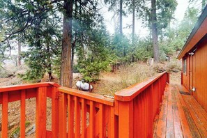 Une terrasse en bois avec une rambarde rouge, entourée d’arbres et d’une petite cabane.