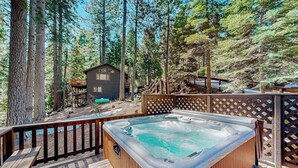 A hot tub on a wooden deck surrounded by a wooden fence, with a small cabin in the background. - Hot Tub Hideaway - Big Trees Village (Dorrington)