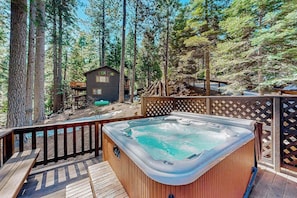 A hot tub on a wooden deck surrounded by a wooden fence, with a small cabin in the background. - Hot Tub Hideaway - Big Trees Village (Dorrington)