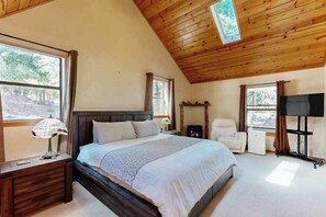 Een slaapkamer met een groot bed, een nachtkastje met een lamp, een stoel, een televisie en een open haard.