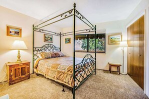 Ein Bett mit Baldachin, ein Holzkopfstück, ein Nachttisch mit Lampe und gerahmte Bilder an den Wänden.