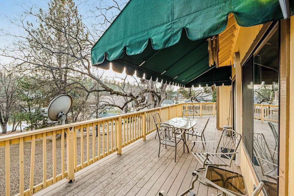 A deck with a yellow railing, a table, and chairs, overlooking a natural landscape with trees and a satellite dish.