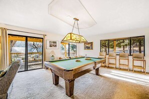 A pool table in a room with a large window, a sofa, and a chair. - Rustic Lakefront Retreat - Pine Mountain Lake (Groveland)