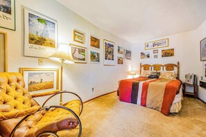 Een slaapkamer met een bed, een stoel en meerdere foto's in lijsten aan de muur.