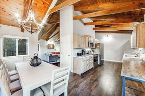 A modern kitchen with wooden beams, a dining area with a table and chairs, and a view of the outdoors. - Wildflower Landing - Pine Mountain Lake (Groveland)