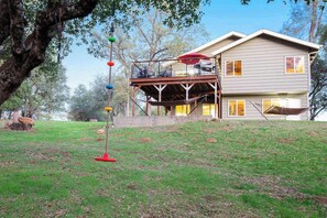 A two-story house with a deck, surrounded by a grassy yard and trees.