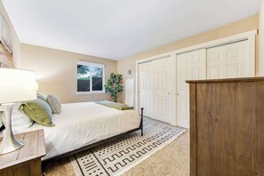 Quarto com cama, mesa de cabeceira, luminária, janela e porta.