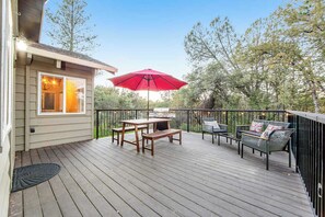 Eine Holzterrasse mit Tisch, Stühlen, einem roten Sonnenschirm und einer Bank.