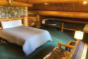 A cabin interior with a large bed, a smaller bed, and a wooden chair.
