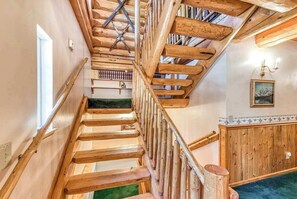 A wooden staircase with a handrail, leading to a room with a green carpet and a wooden wall panel.