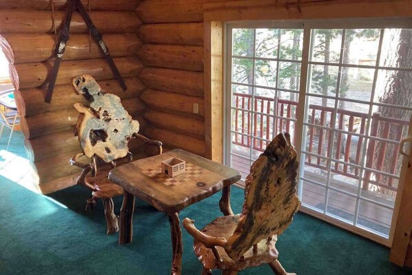 A wooden cabin interior with a large window, a wooden table, and a chair.