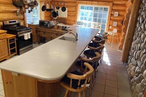 A wooden cabin interior with a kitchen featuring a stove, oven, microwave, and a long counter with stools.