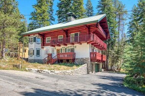 A two-story log cabin with a balcony, surrounded by forest.