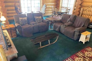 A log cabin interior with a sofa set, a wooden sled, and a dining area with chairs.