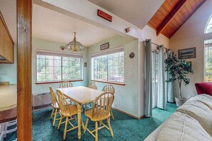 Un comedor con mesa y sillas de madera, ventanas amplias y techo con vigas a la vista.