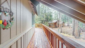 Eine Holzdielen-Terrasse mit Geländer, einem Willkommensschild und Blick auf eine bewaldete Landschaft mit einer Holzhütte.