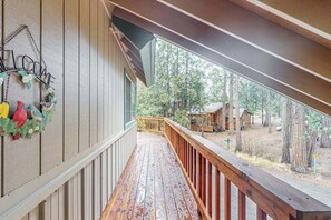 Eine Holzdielen-Terrasse mit Geländer, einem Willkommensschild und Blick auf eine bewaldete Landschaft mit einer Holzhütte.