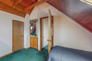 A room with a sloped ceiling, a bed, a wardrobe, and a door leading to another room. - Traveler's Rest - East Village (Shaver Lake)