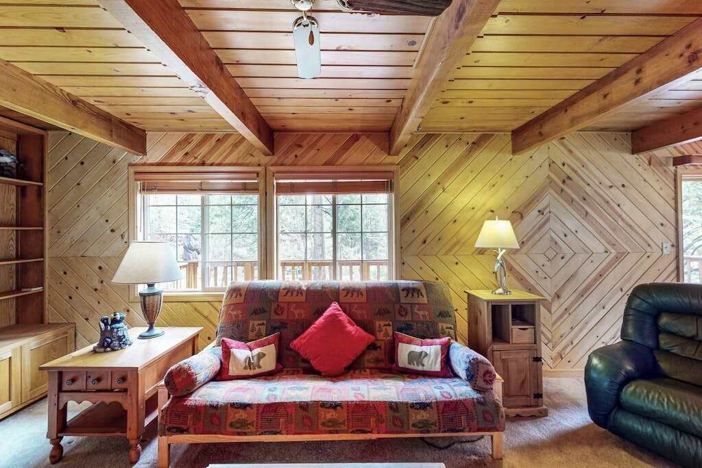 Una habitación acogedora con techo de madera, un sofá con cojines estampados, una lámpara y una silla.