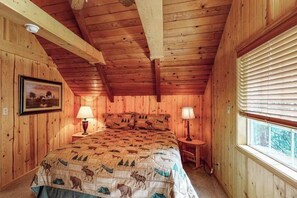 Ein Zimmer mit Holzwandverkleidung, einem Bett, zwei Nachttischlampen, einem Fenster mit Jalousien und einem gerahmten Bild an der Wand.