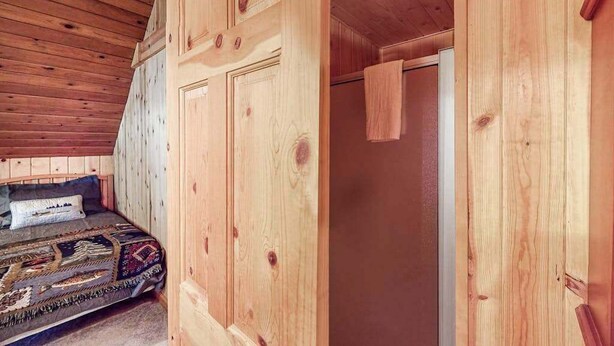 A wooden interior with a bed, a door, and a sloped ceiling. - The Dollhouse Cabin - Blue Lake Springs (Arnold)
