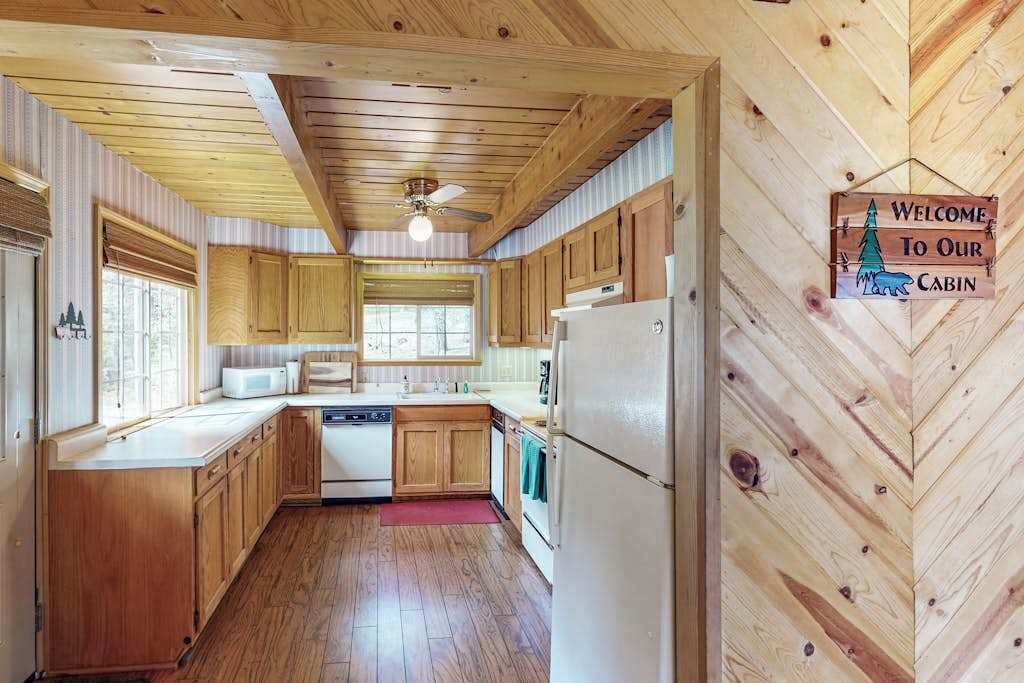 A cabin interior with wooden walls, a kitchen area including a microwave, sink, and refrigerator, and a ceiling fan.