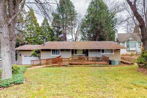 Ein Bungalow mit Veranda, Garage und einem Garten mit Bäumen.
