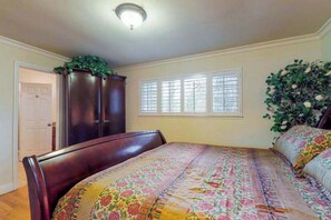 Ein Schlafzimmer mit Bett, Kleiderschrank, Fenster mit Jalousien und einer Tür.