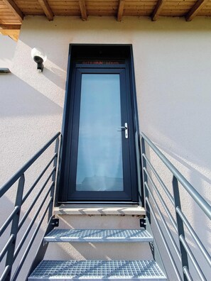 A black-framed door with a glass panel, a metal handrail, and a metal staircase leading to it.