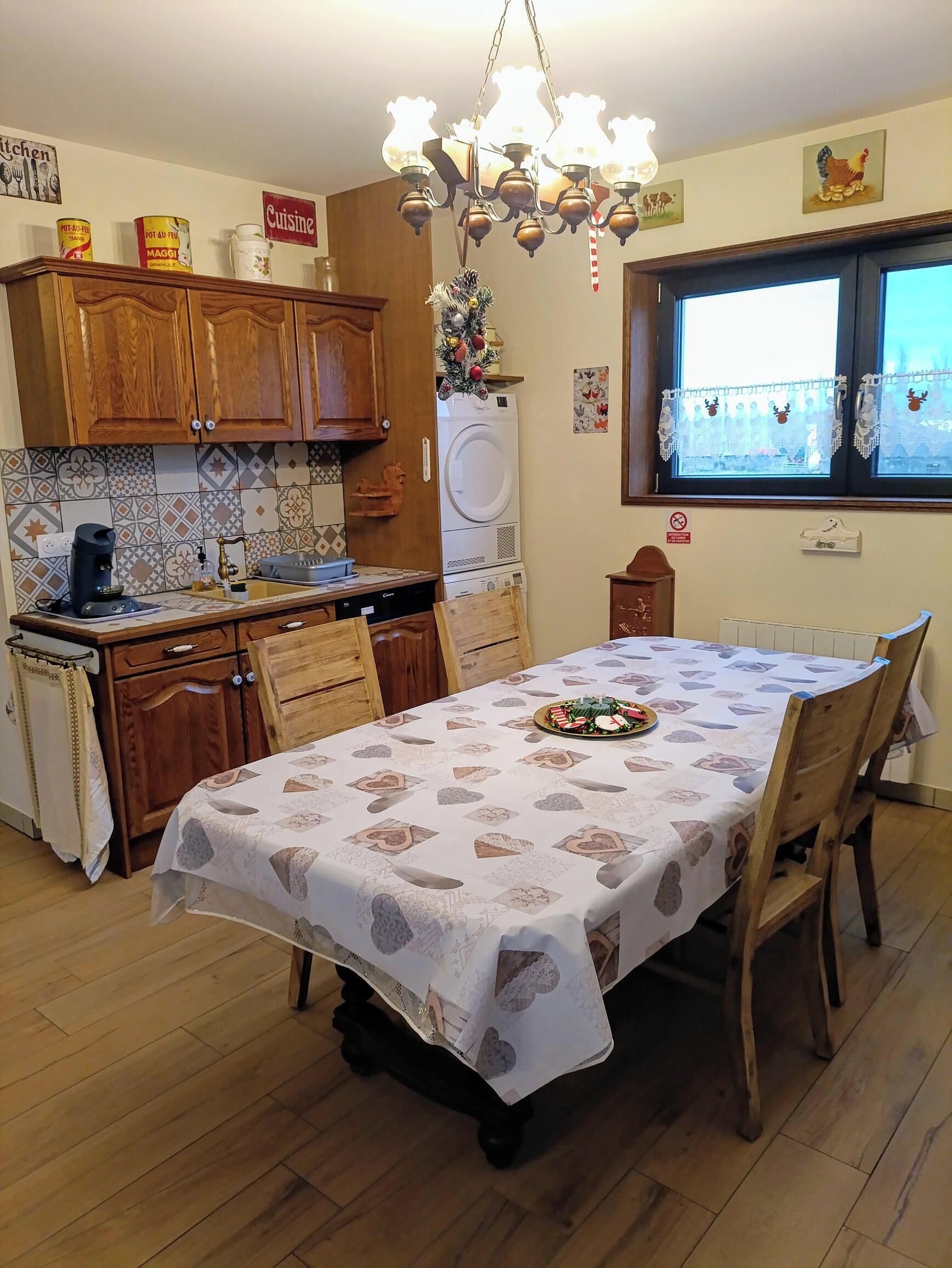 A dining area with a table set for four, a kitchen with wooden cabinets, a coffee machine, and a washing machine.