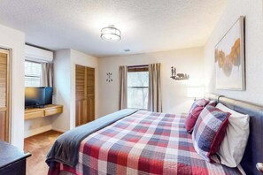 A bedroom with a bed, a television on a stand, a desk, and a window. - Creekside Cabin - Pine Mountain Lake (Groveland)