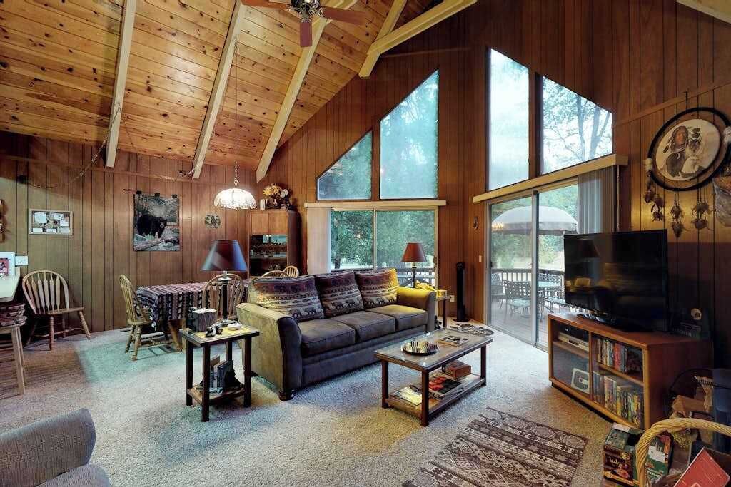 Un salon chaleureux avec un canapé, une table basse et un téléviseur, de grandes fenêtres et des murs en bois.
