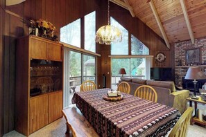 A cozy cabin interior with a dining table, wooden chairs, a bench, a fireplace, and a large window. - Bear's Meadow - Meadowmont (Arnold)