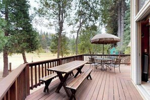 Eine Holzterrasse mit Picknicktischen und -stühlen, umgeben von Bäumen.