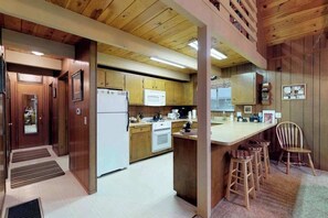 A kitchen with wooden cabinets, a white refrigerator, a microwave, and a stove. There is a small bar area with stools. - Bear's Meadow - Meadowmont (Arnold)