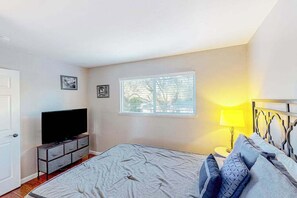 Une chambre à coucher avec un lit, un téléviseur posé sur un meuble, une fenêtre avec des stores et une lampe de chevet.