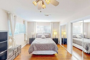 A bedroom with a bed, bedside tables, a dresser, a ceiling fan, and a large mirror.