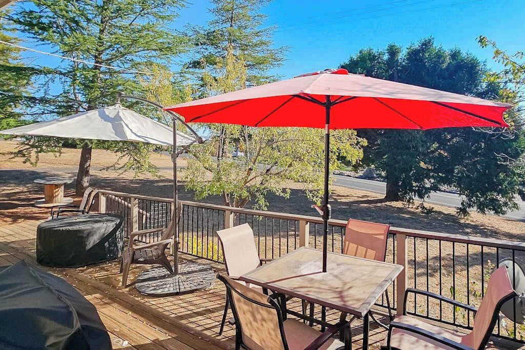 Um pátio externo com mesa, cadeiras, churrasqueira e um guarda-sol vermelho.