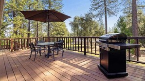 Eine Holzterrasse mit Grill, Tisch, Stühlen und Sonnenschirm.