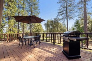 Eine Holzterrasse mit Grill, Tisch, Stühlen und Sonnenschirm.