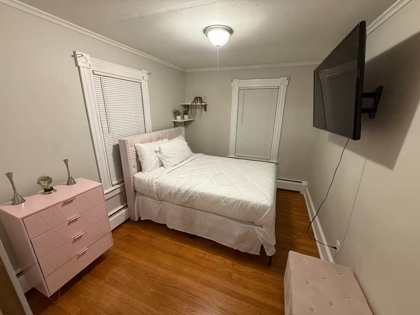 A bedroom with a bed, a dresser, a TV, and two windows with shutters.