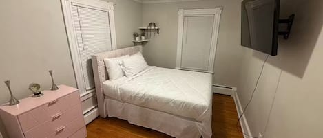 A bedroom with a bed, a dresser, a TV, and two windows with shutters.