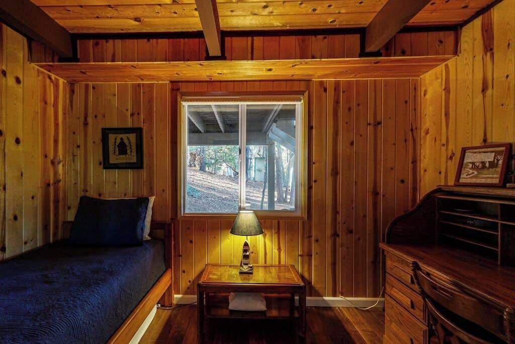 Une pièce de cabane en bois comprenant un lit, une table avec une lampe, une fenêtre et une commode.