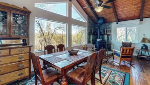 Un comedor con mesa y sillas de madera, chimenea y ventanas amplias.