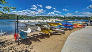 Varias canoas y kayaks alineados en un muelle de hormigón junto a un lago tranquilo.