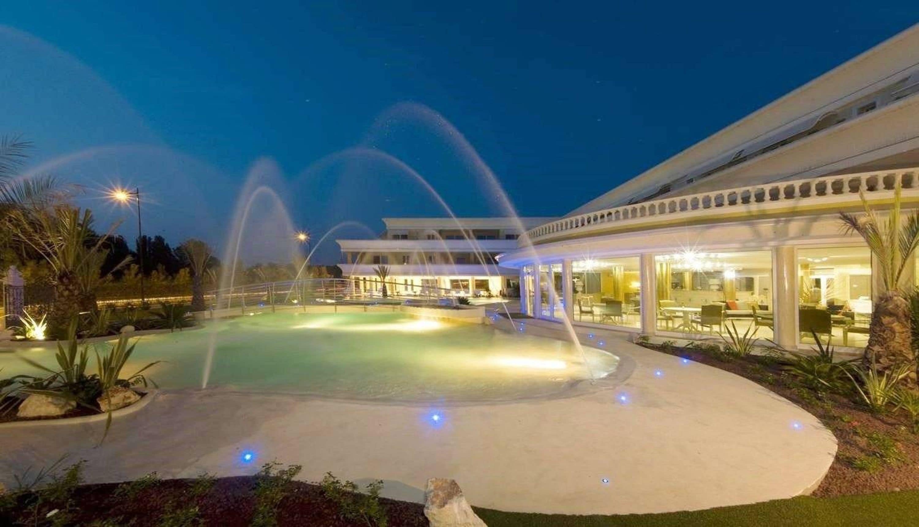 Een goed verlicht buitenzwembadgedeelte met waterpartijen en een gebouw met grote ramen.